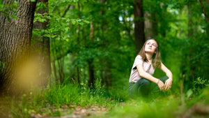 Young woman looking up at the trees in a crouching position - nature-themed indoor and outdoor activities for summer. 