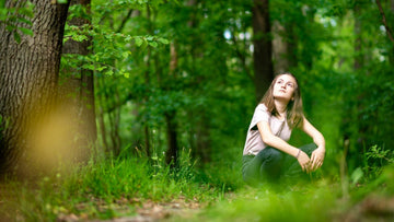 Young woman looking up at the trees in a crouching position - nature-themed indoor and outdoor activities for summer. 