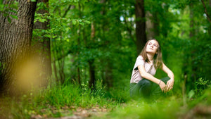 Young woman looking up at the trees in a crouching position - nature-themed indoor and outdoor activities for summer. 