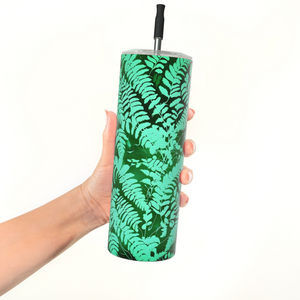 A hand holding a tall insulated tumbler with a green fern leaf pattern and a black straw, against a plain white background - Fern Tumbler - Stainless Steel - Spruce and Heron.