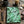 A spiral-bound notebook from Spruce and Heron with a green fern leaf pattern lies on a rustic wooden table, surrounded by lifestyle props including a ceramic mug of coffee, a candle, a pen, a pencil, a small compass, and a leather journal.