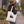 A woman wearing a brown wide-brim hat, dark green sweater, and blue jeans walks on a campus path carrying a white canvas tote bag with a black tree graphic - Spruce Trees Tote Bag from Spruce and Heron.