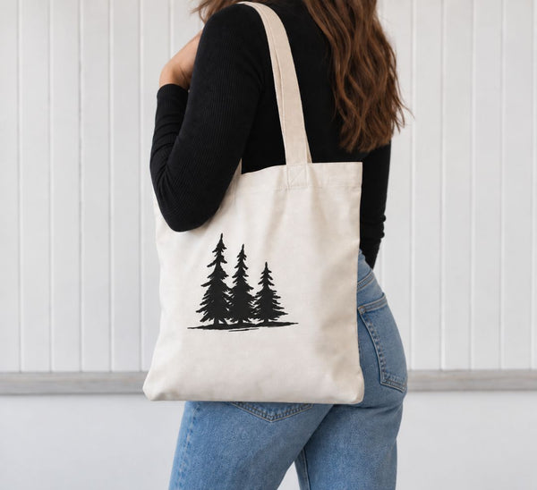 A woman from the back wearing a black long-sleeve top and blue jeans, carrying a natural canvas tote bag with a black pine tree graphic on a white paneled wall background - tote bag from Spruce and Heron.